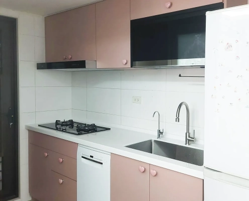 乾燥玫瑰色系統廚具完工正面全景，搭配溫潤木質調與現代化廚房家電，完美展現優雅美學與日常收納機能