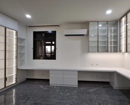 工作室全景設計，超長 L 型工作桌整合左側落地除濕高櫃與右側除濕防潮吊櫃，實現手辦展示與海量收納一體化