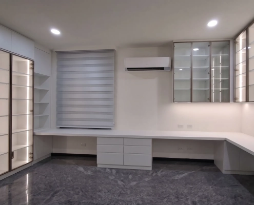工作室全景設計，超長 L 型工作桌整合左側落地除濕高櫃與右側除濕防潮吊櫃，實現手辦展示與海量收納一體化
