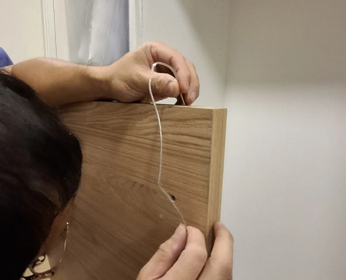 除濕防潮精品展示櫃現場施工紀錄：師傅於衣櫃側板進行精準引線作業，落實隱蔽式電源配線與客製結構嵌合工法。